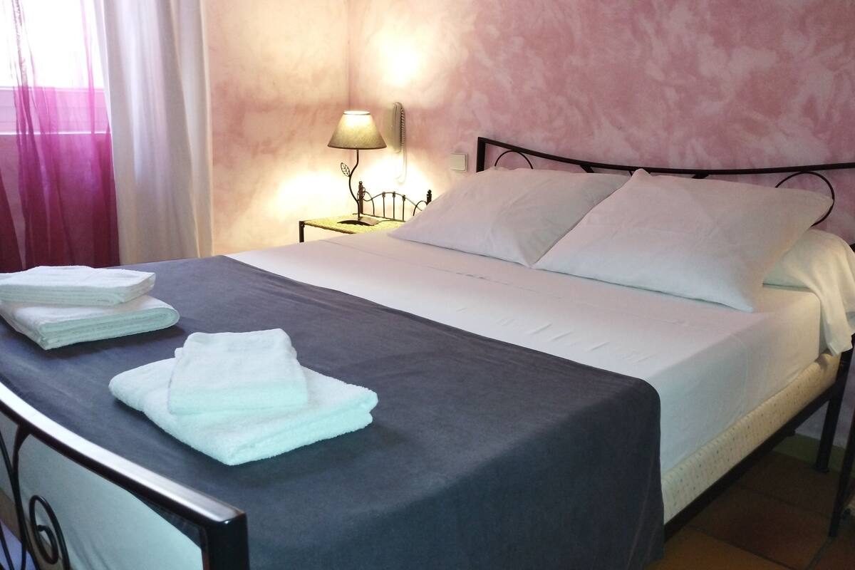 Een net opgemaakt bed met witte lakens, een bedlamp en een wandradiator.