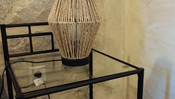 Une table à plateau en verre sur laquelle repose une lampe en osier, le tout placé devant un mur en pierre.