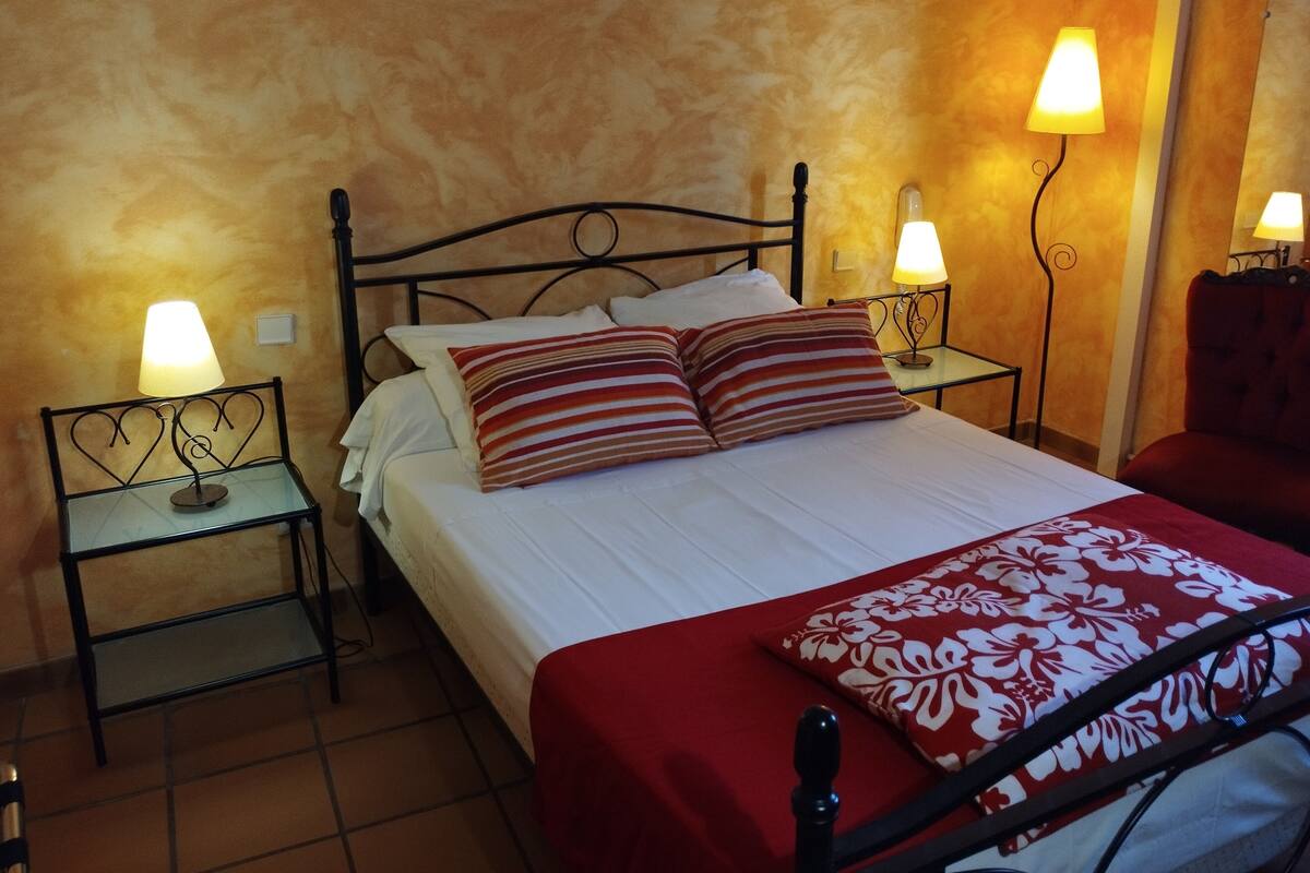 Hotelkamer met een bed, twee nachtkastjes met lampen, een rode en witte gestreepte plaid en een rode stoel.