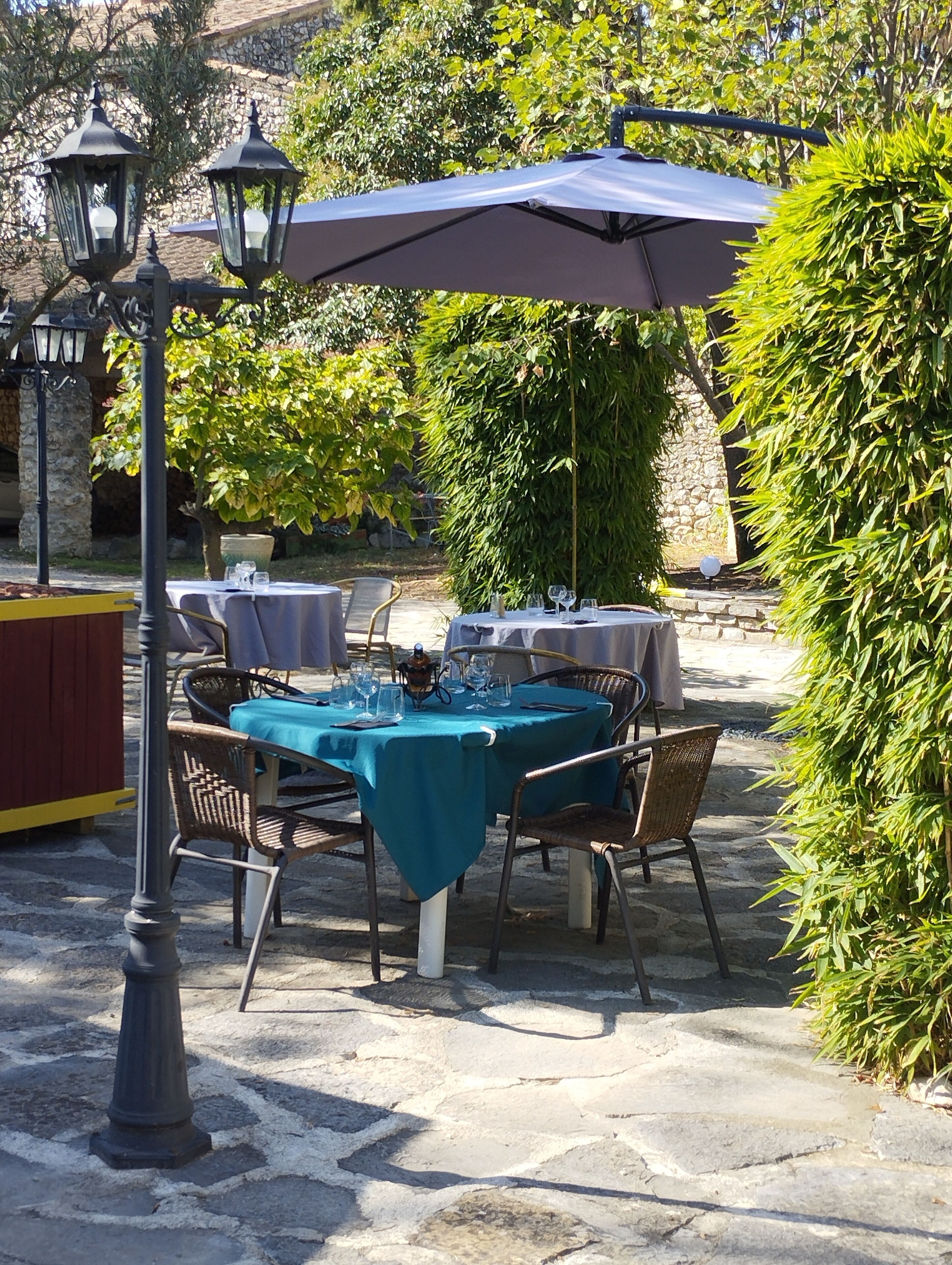 Un espace de restauration en plein air avec des tables pour deux, entouré de verdure et de murs en pierre.