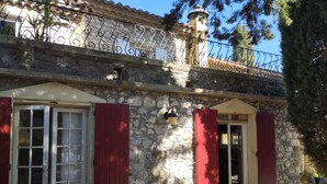 Un bâtiment en pierre avec des volets rouges, un balcon doté d’une balustrade en fer forgé et un petit porche.