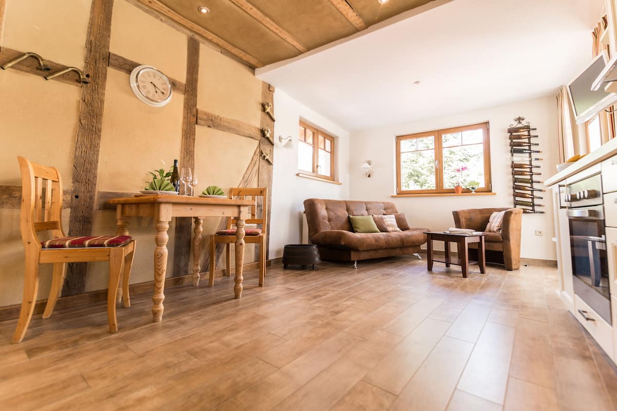 A spacious living area with a wooden dining table, two chairs, a brown sofa, and a television.