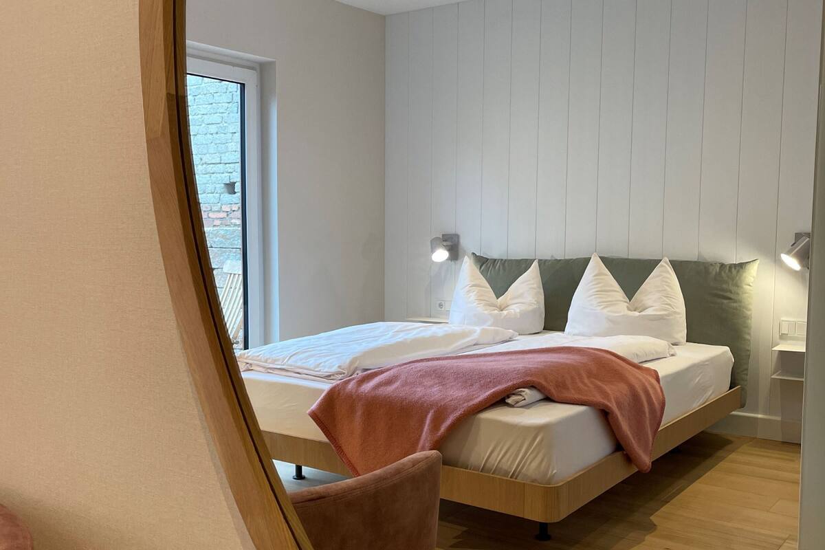 A modern bedroom with a bed, bedside tables, and a view through a window.