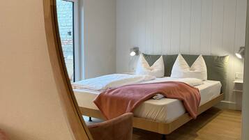 A modern bedroom with a bed, bedside tables, and a view through a window.