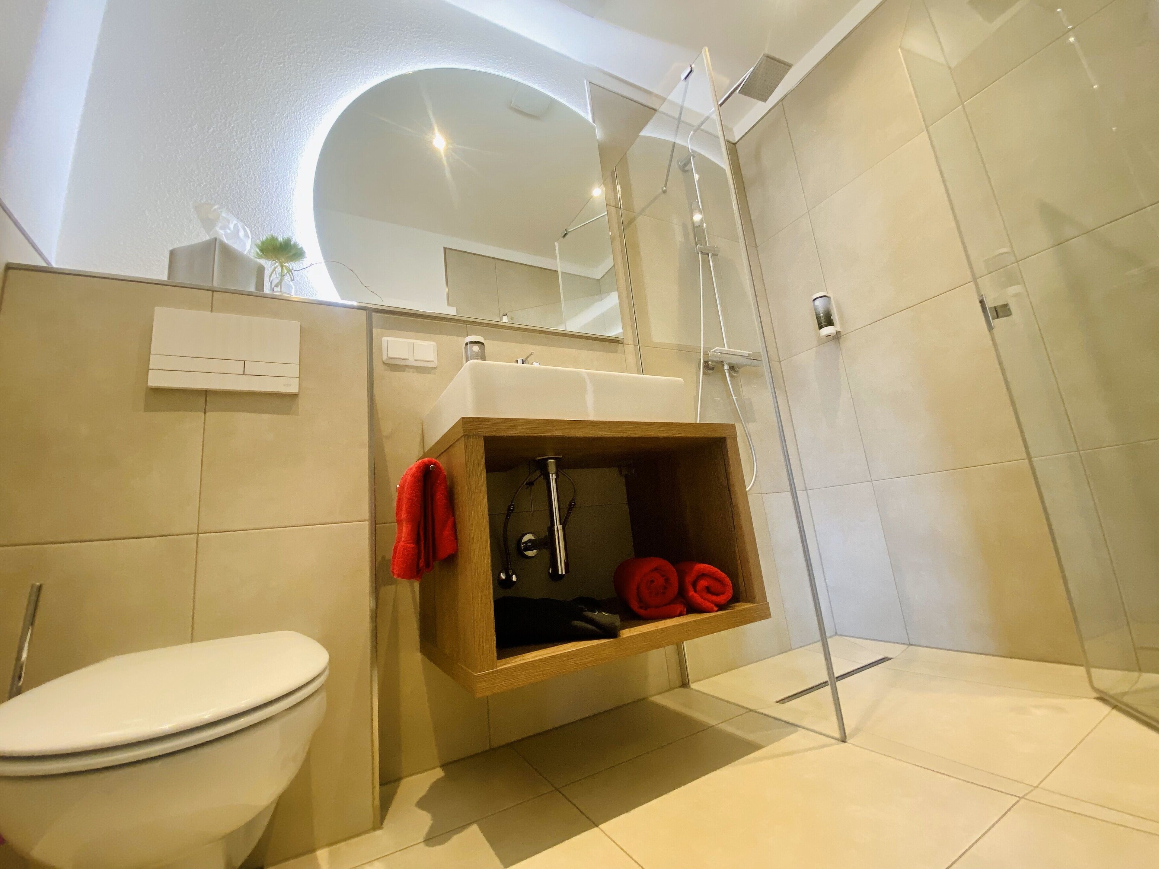 Ein modernes Badezimmer mit Toilette, Waschbecken, Dusche und einer Holzeinrichtung mit roten Handtüchern.