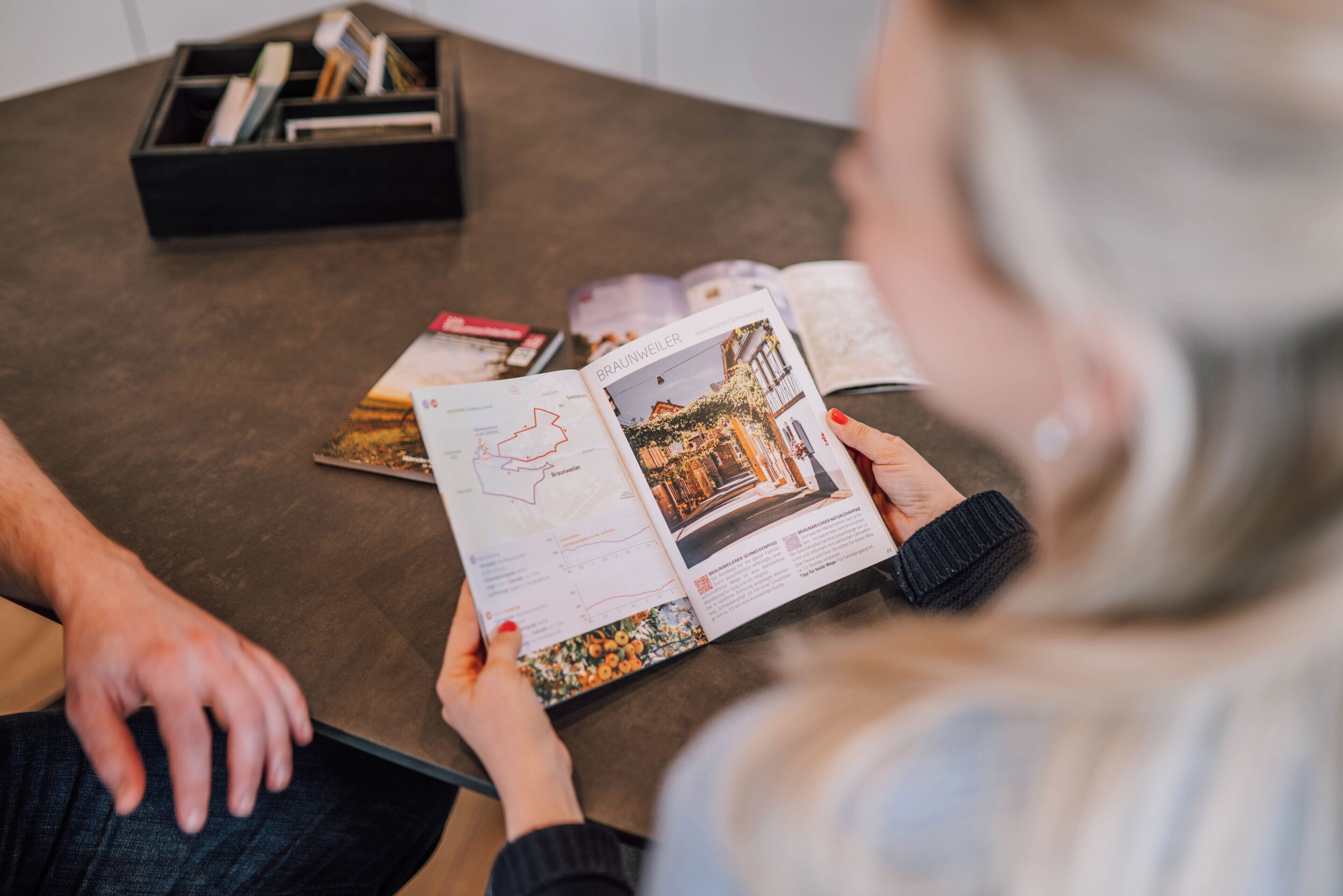 A person reading a magazine with a map and an article on a table.
