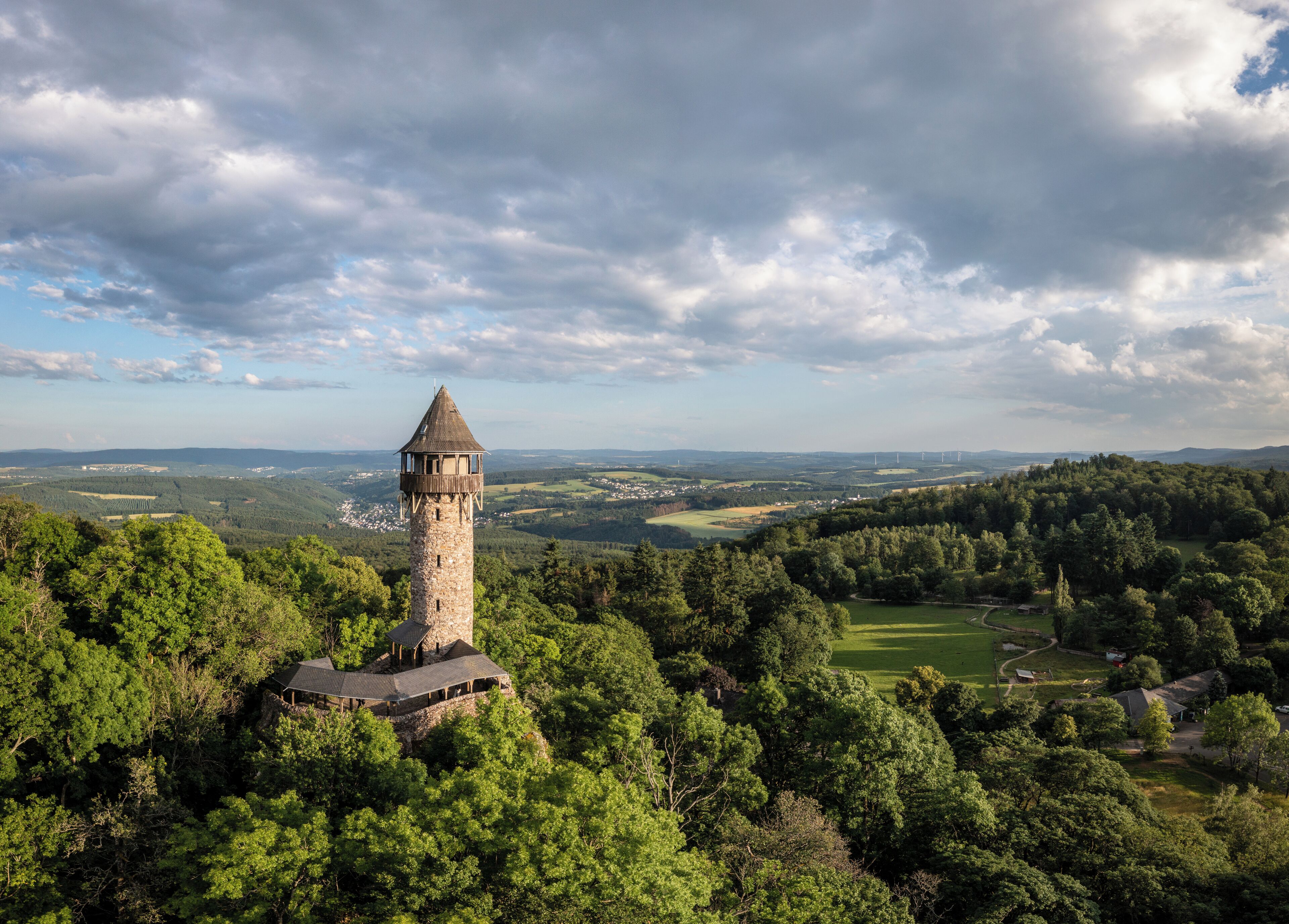 Une tour entourée d’une forêt dense, dominant une vallée où l’on aperçoit une petite ville au loin.