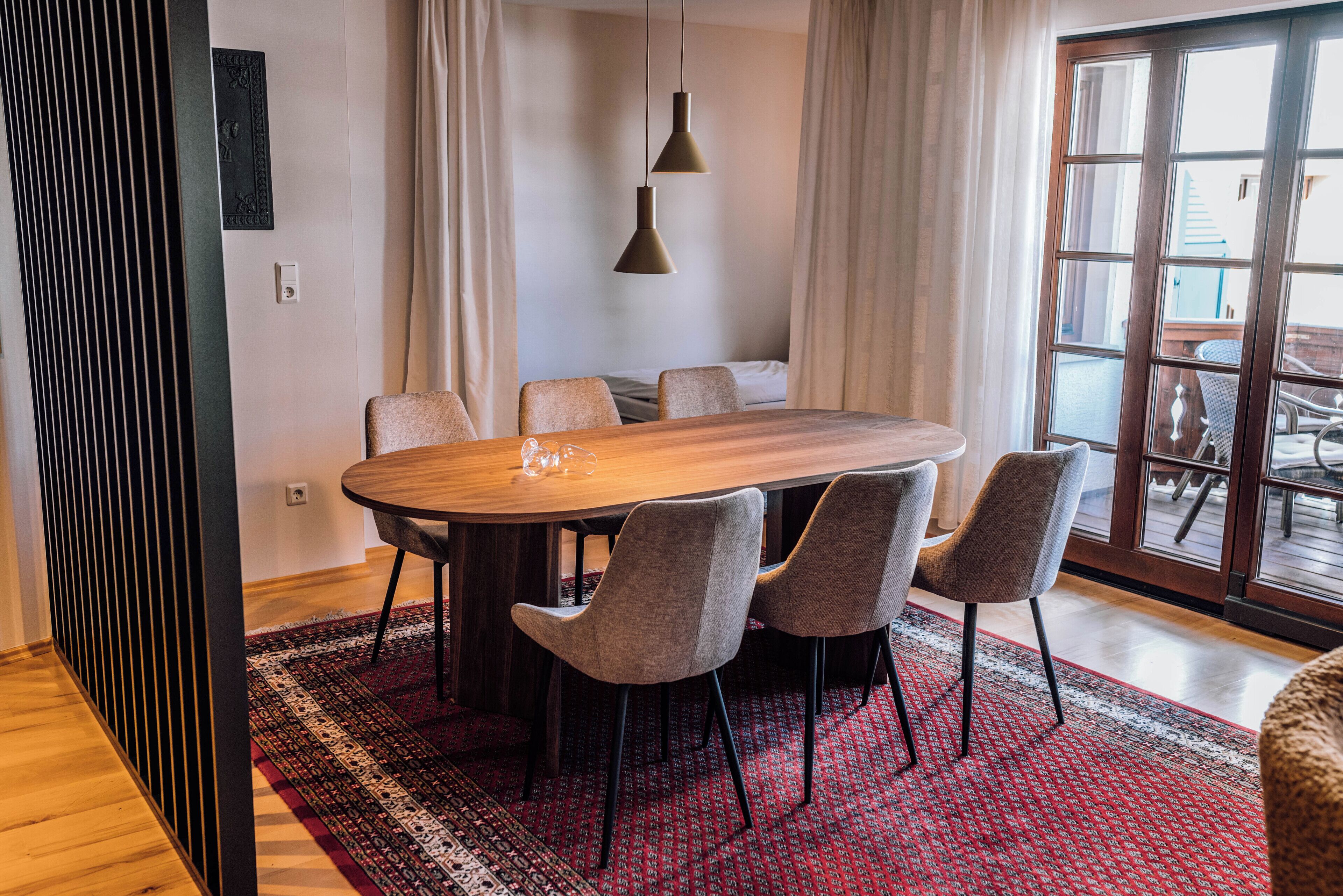 A dining area with a wooden table and six chairs, a patterned rug, and a view through a glass door to an outdoor area.