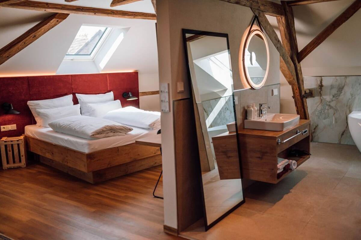 A bedroom with a wooden bed, a red headboard, a skylight, a large mirror, and a bathroom with a marble wall and wooden vanity.