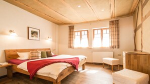 A bedroom with a wooden bed, a bedside table, a chair, and a window with curtains. - Schmidtburger Hof (Weiler bei Monzingen)