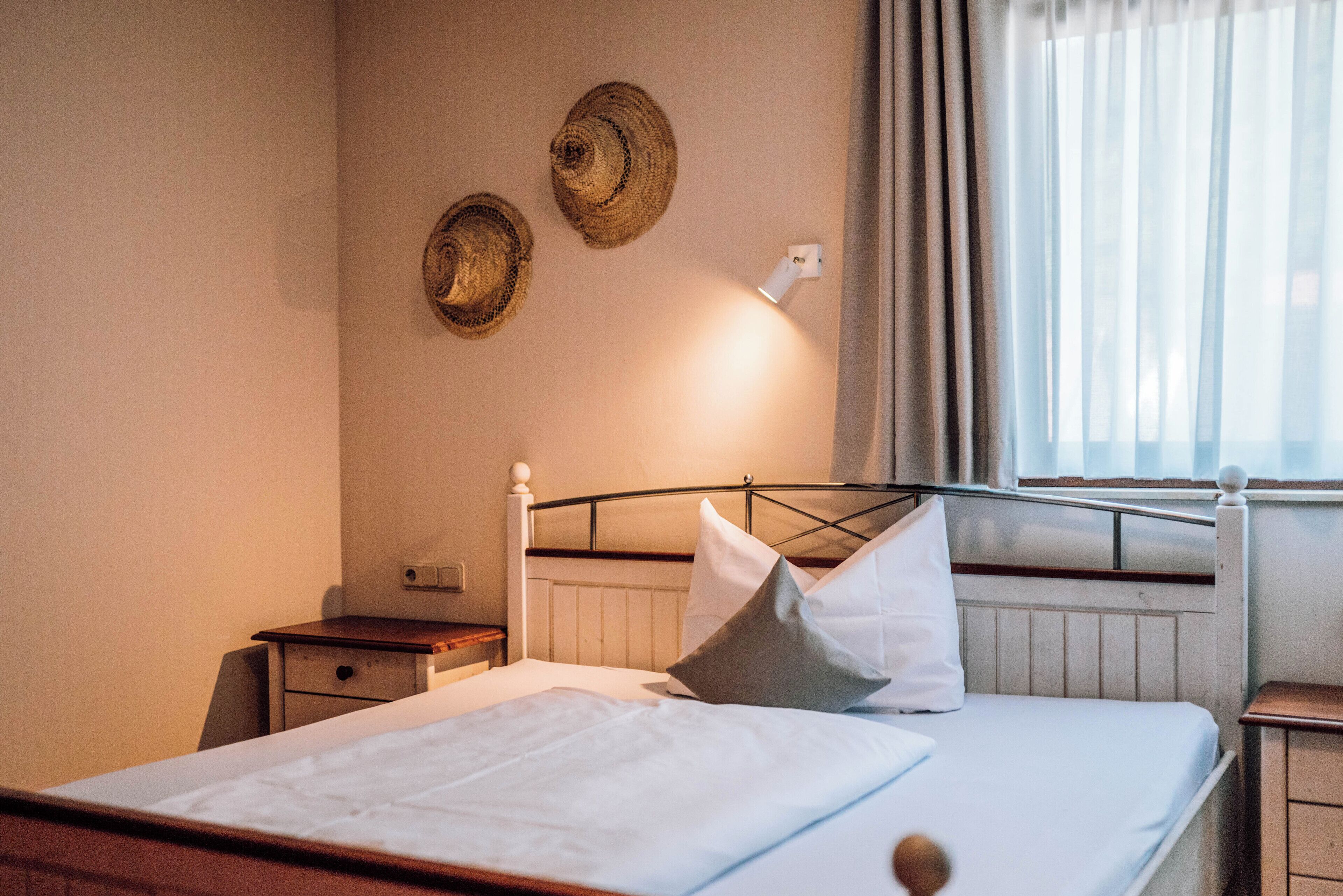 A neatly made bed with white linens, a wooden headboard, and a bedside table with a lamp.