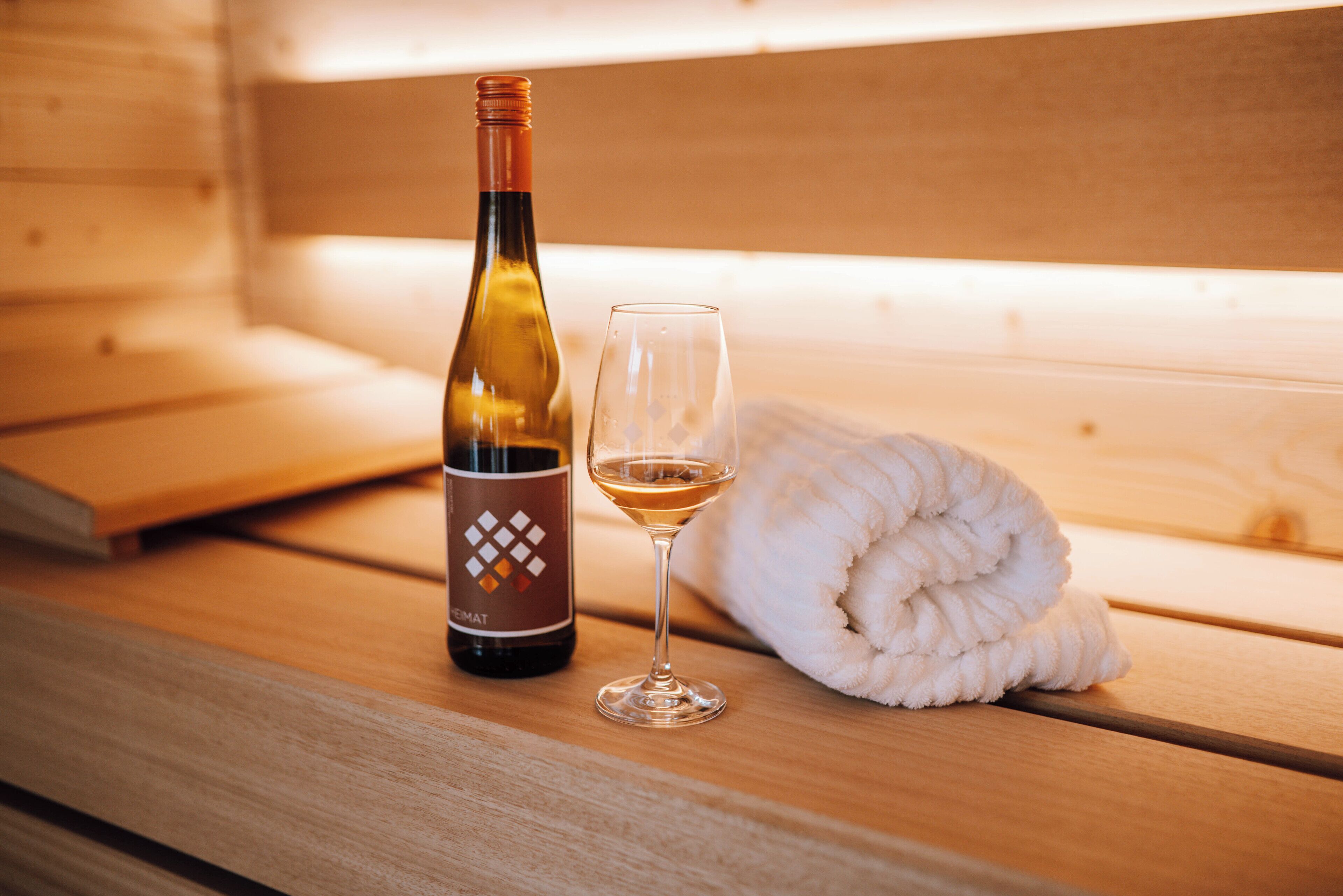 A bottle of wine and a glass on a wooden bench with a white towel.
