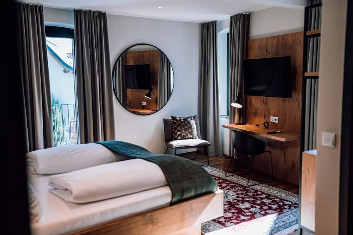 A hotel room with a bed, a desk, a chair, a TV, and a large mirror.
