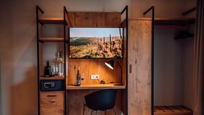 Una camera da letto compatta e moderna, con una scrivania in legno, una sedia, una TV e un armadio.