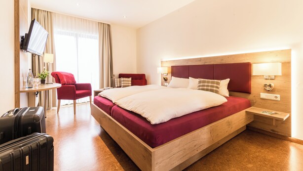 A hotel room with a wooden bed, a desk, a chair, and a TV. - Schmidtburger Hof (Weiler bei Monzingen)