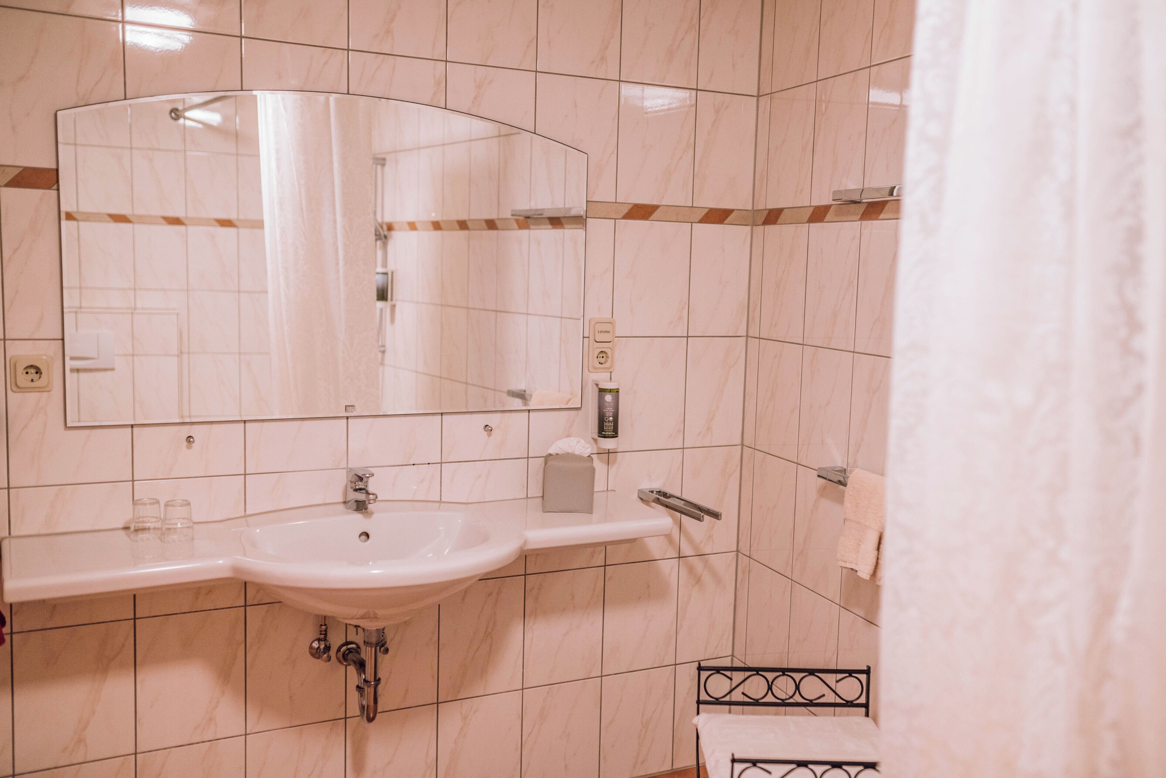 A bathroom with a sink, mirror, towel rack, and shower curtain.