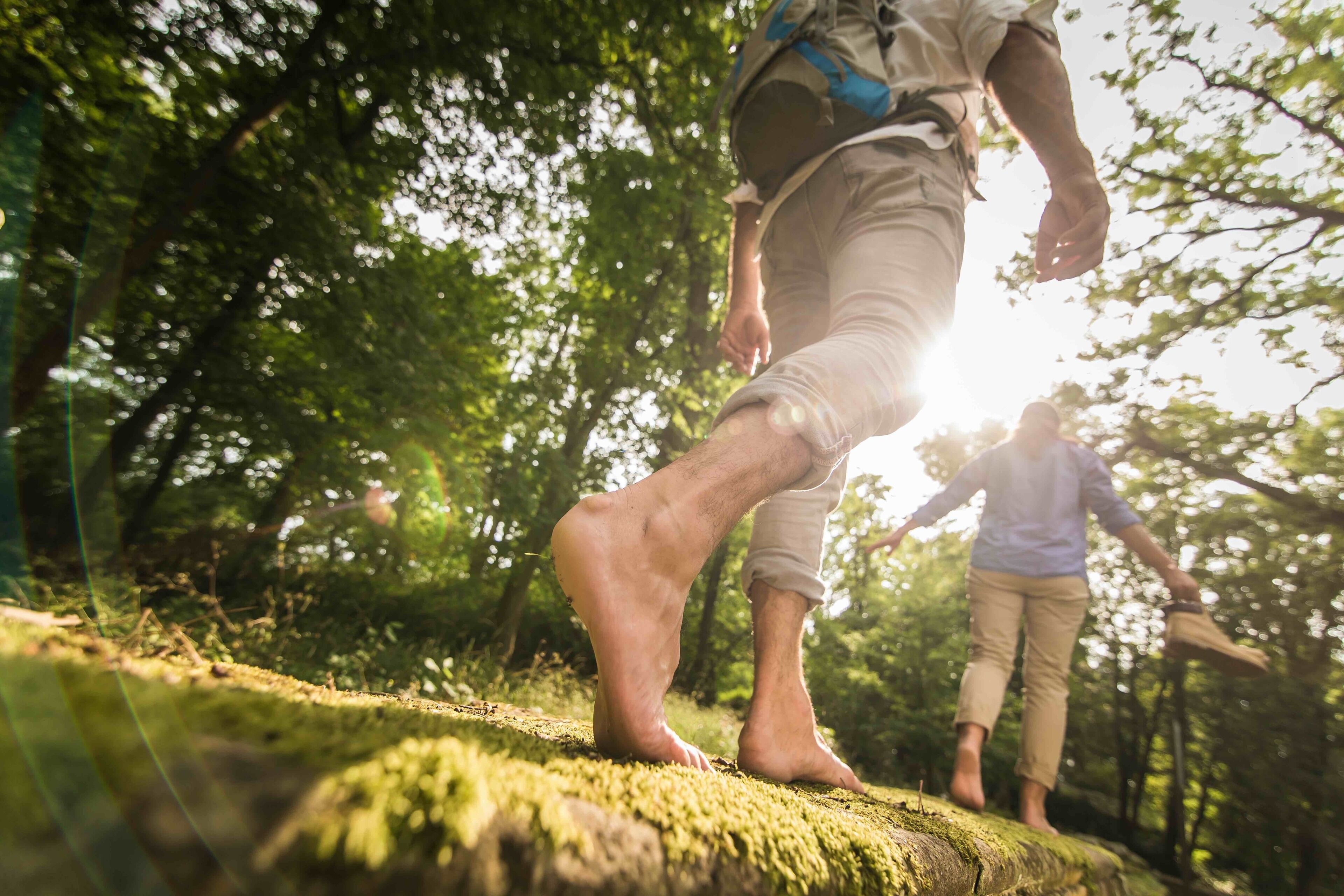 A person walking barefoot on a moss-covered rock in a forest.