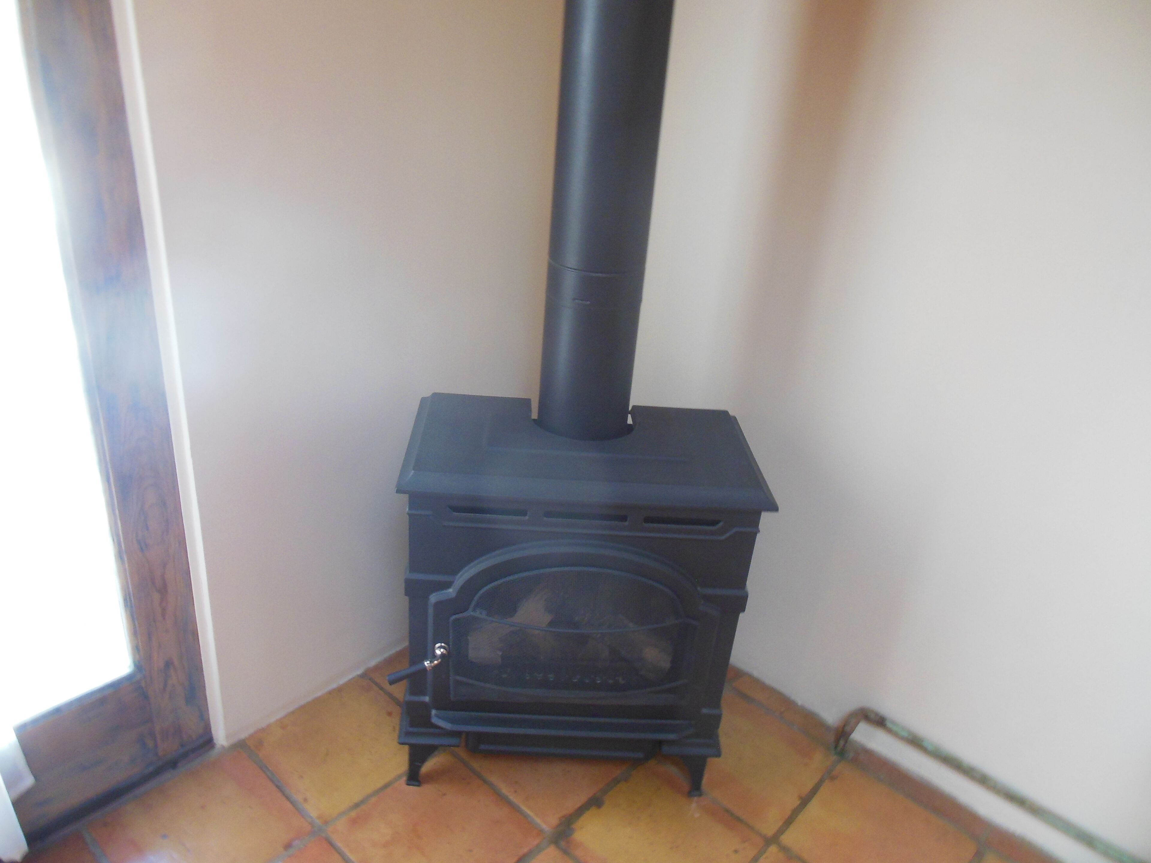 A black wood-burning stove with a chimney, positioned in a corner with tiled flooring.