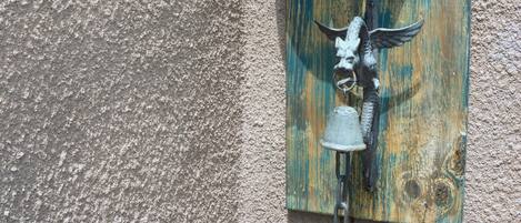 A blue bell mounted on a textured wall, attached to a wooden board with a metal hook.