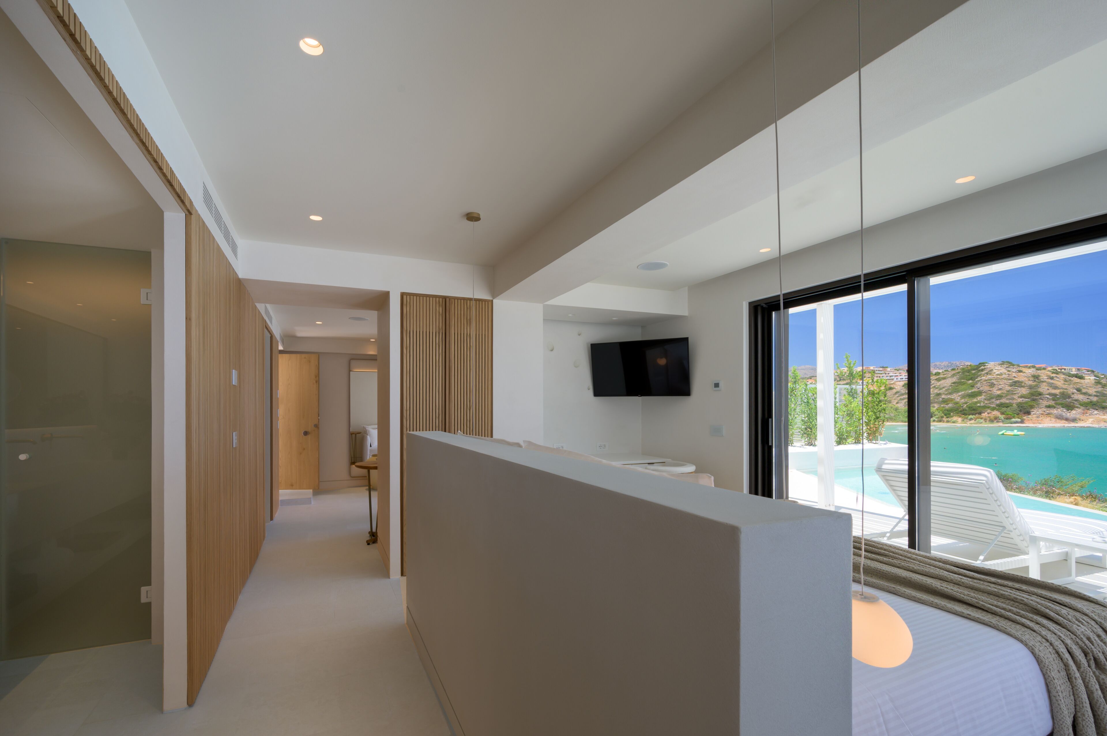 A modern hotel room with a large window, a TV, and a view of the sea.