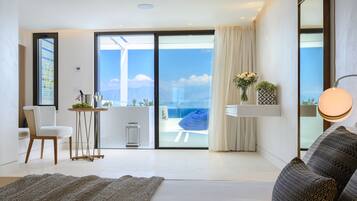 Una habitación de hotel moderna con un gran ventanal corredera que da a un balcón con vistas al mar y a las montañas.
