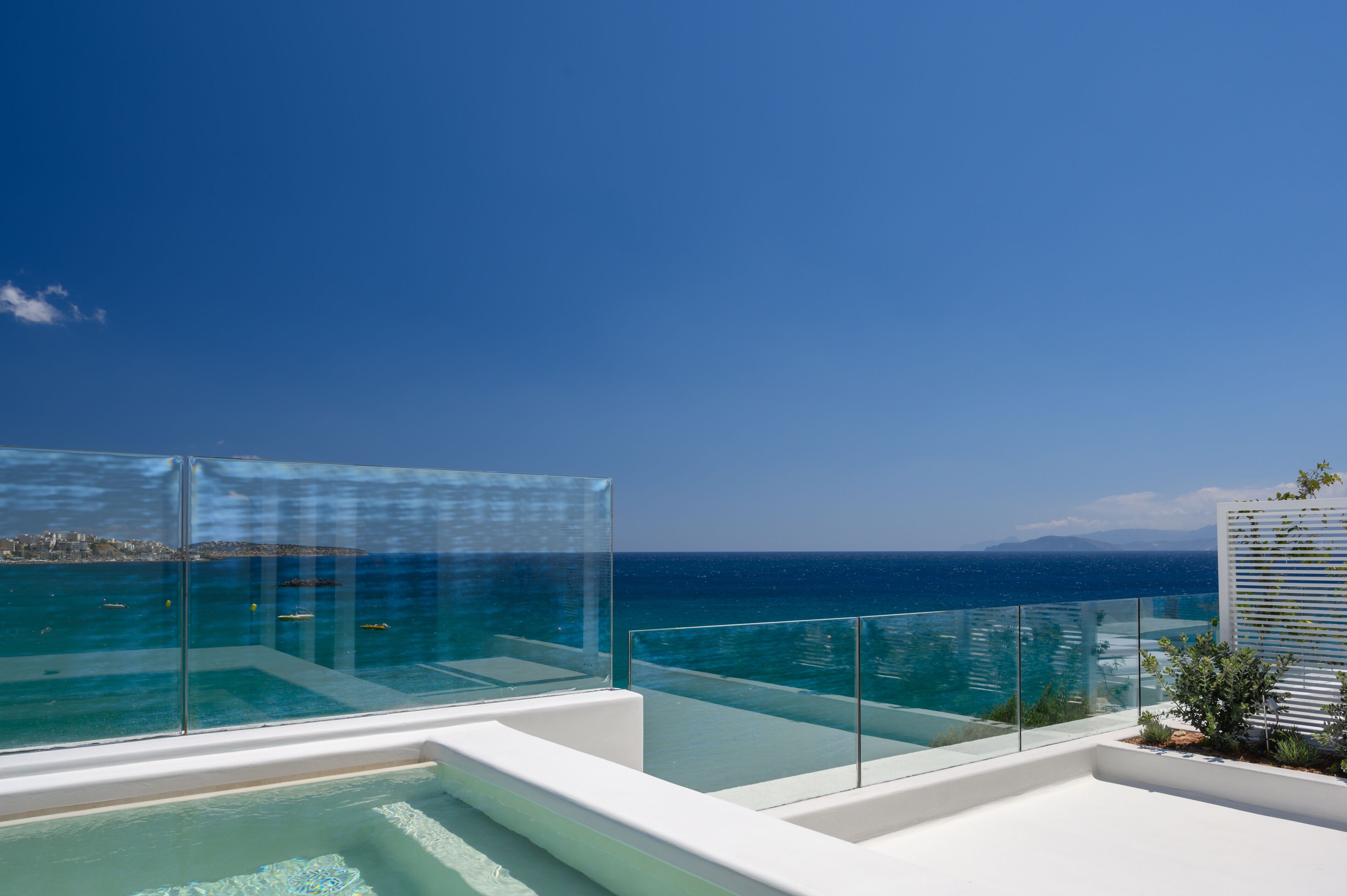Una piscina infinita moderna con barandillas de vidrio transparente, con vistas al mar tranquilo y a la costa distante.