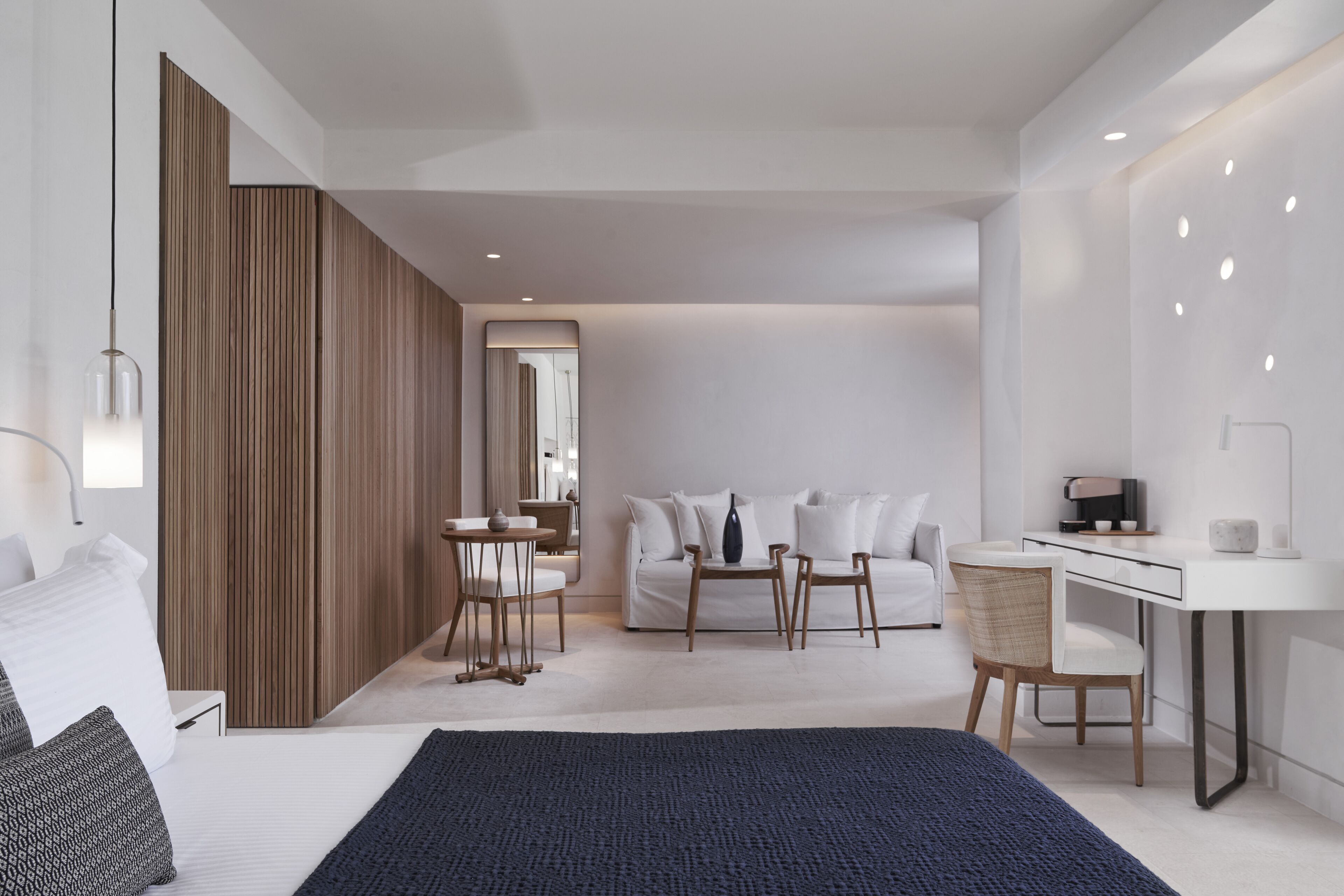 Moderni hotellihuone, jossa on sänky, työpöytä, tuoli, sohva ja puinen sermi.