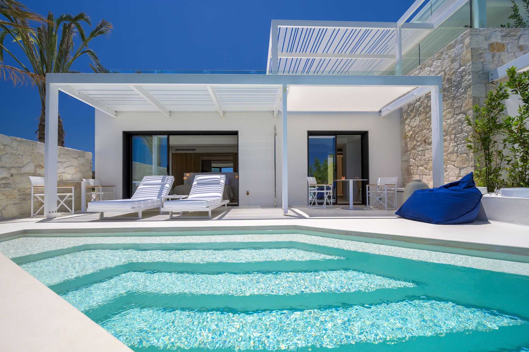 Un área de piscina moderna con sillones de descanso y un asiento tipo sillón de forma redondeada azul.