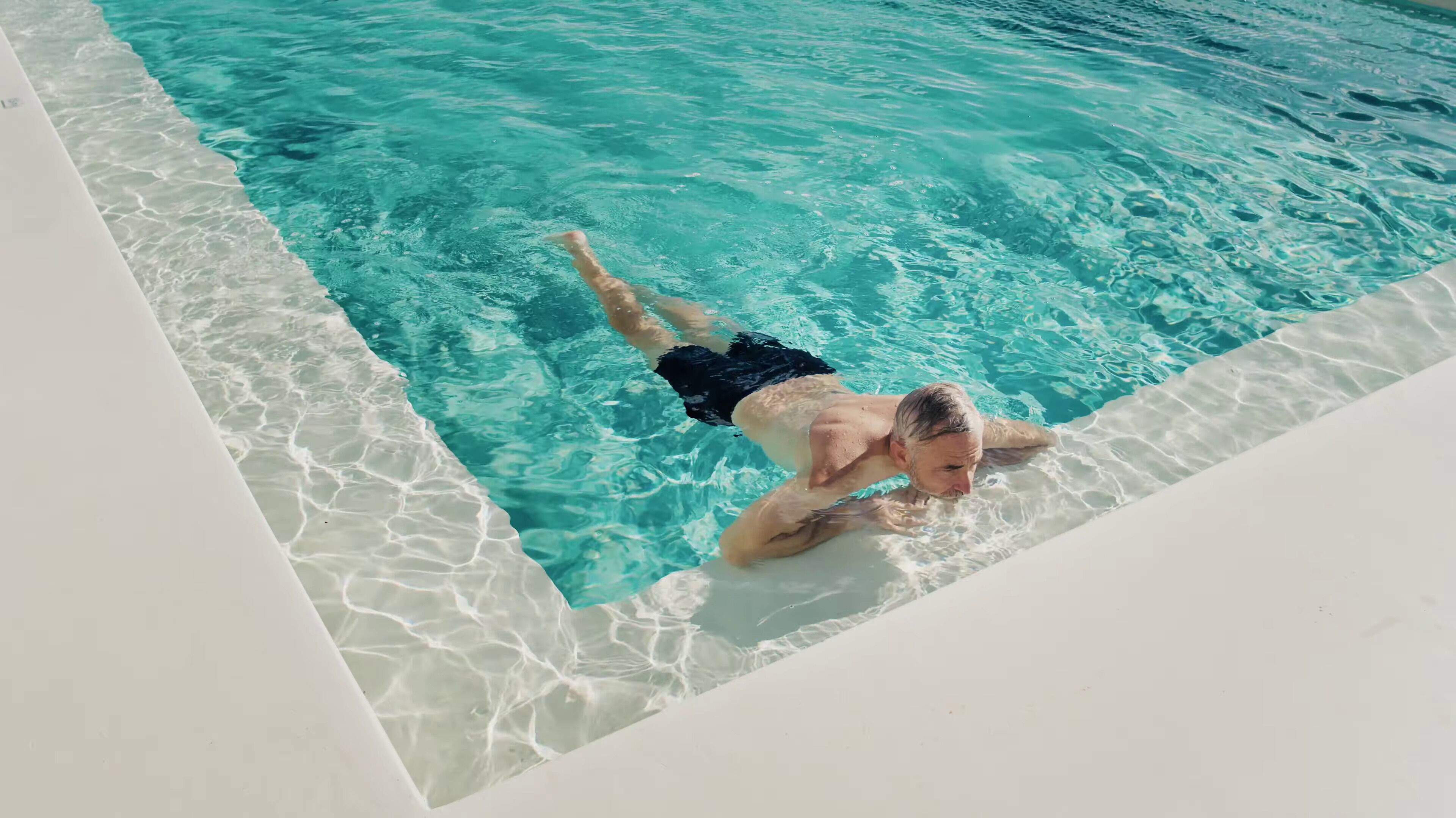 Una persona nadando en una piscina azul cristalina con borde blanco.