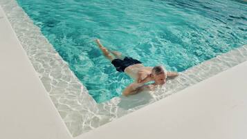 Una persona nadando en una piscina azul cristalina con borde blanco.