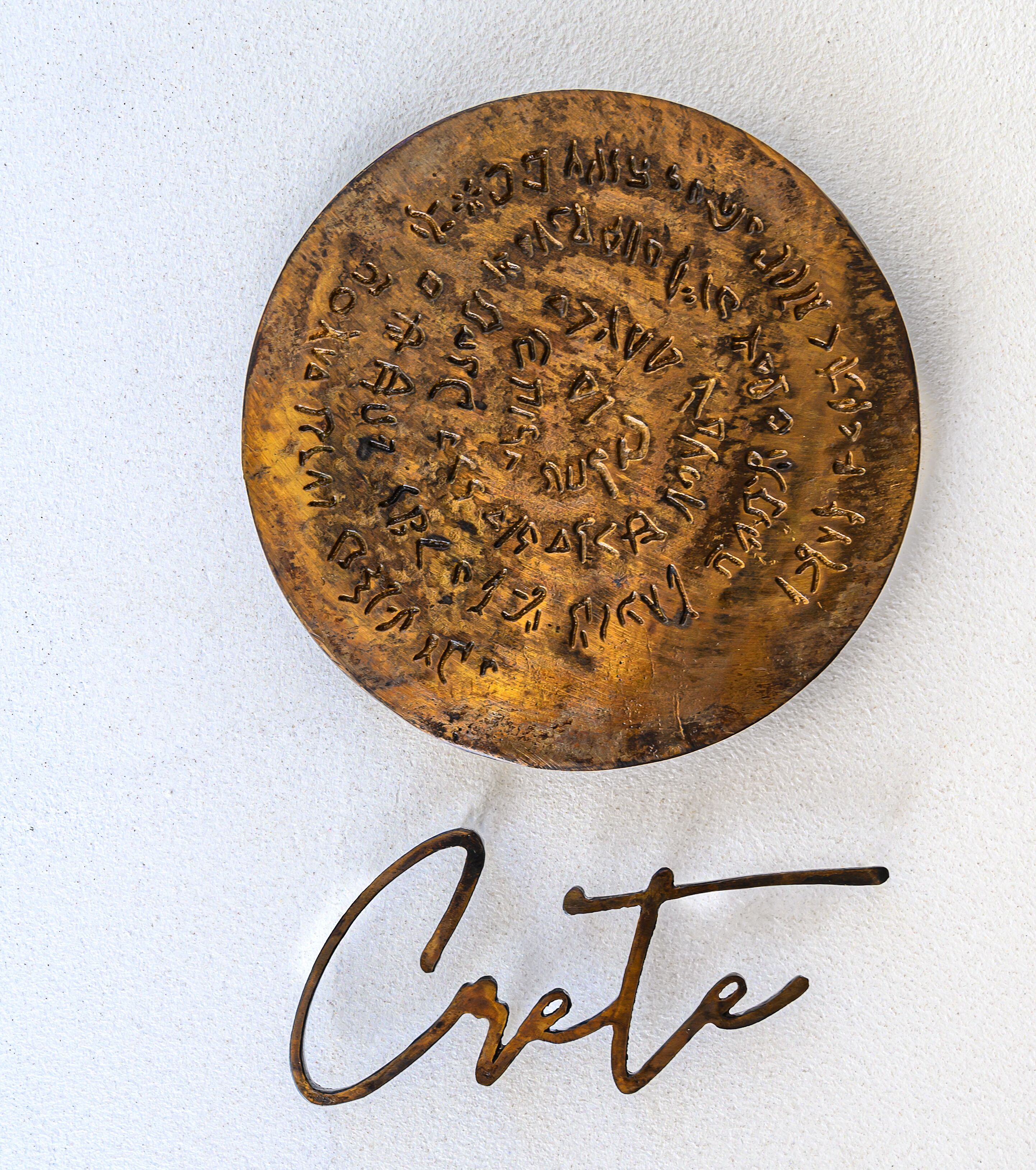 Eine runde Metalltafel mit hebräischen Inschriften und dem Wort 'Crete' darunter.