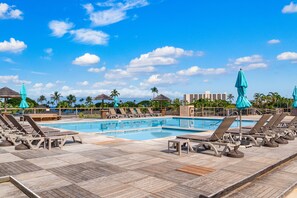 A poolside area with lounge chairs and umbrellas, a clear sky, and a view of the ocean.