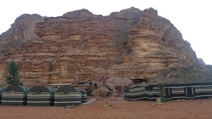 A large rock formation with a series of tents in the foreground. - Wadi rum light camp (Wadi Rum)