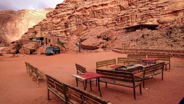 A desert setting with a stone building, wooden benches, and tables arranged for dining. - Wadi rum light camp (Wadi Rum)
