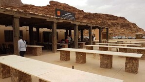 An outdoor seating area with stone tables and benches, a covered shelter, and a sign welcoming visitors to the Wadi Rum Desert Hotel. - Wadi rum light camp (Wadi Rum)