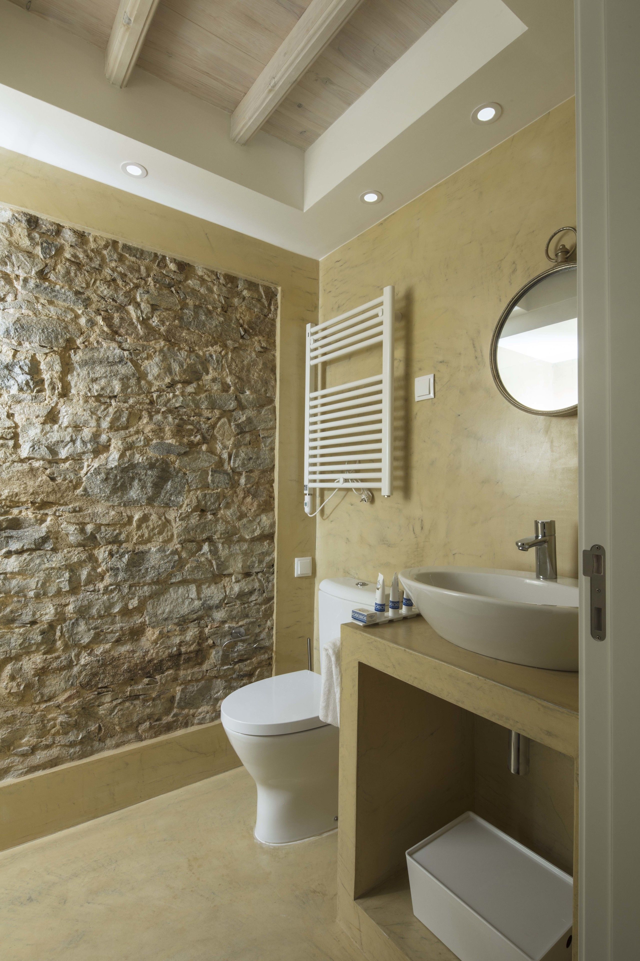 A bathroom with a stone wall, a white toilet, a sink, and a mirror.