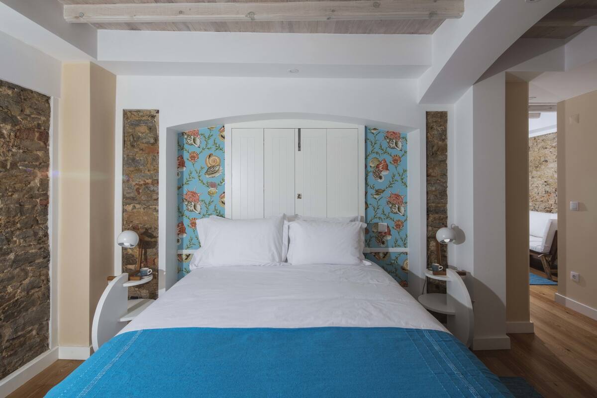 A bedroom with a bed, white walls, and a stone accent wall.