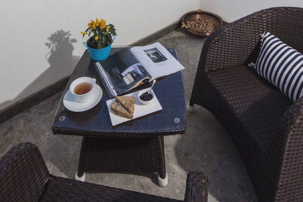 A balcony with wicker furniture, a table with a book, a cup of tea, and a bowl of nuts.