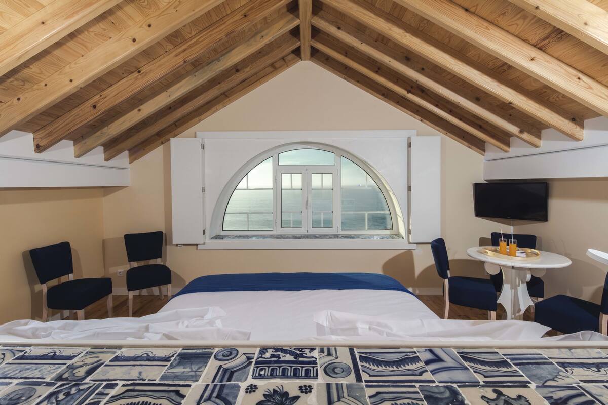 A bedroom with a large bed, a window with a view, a small table with a tray, and a TV mounted on the wall.