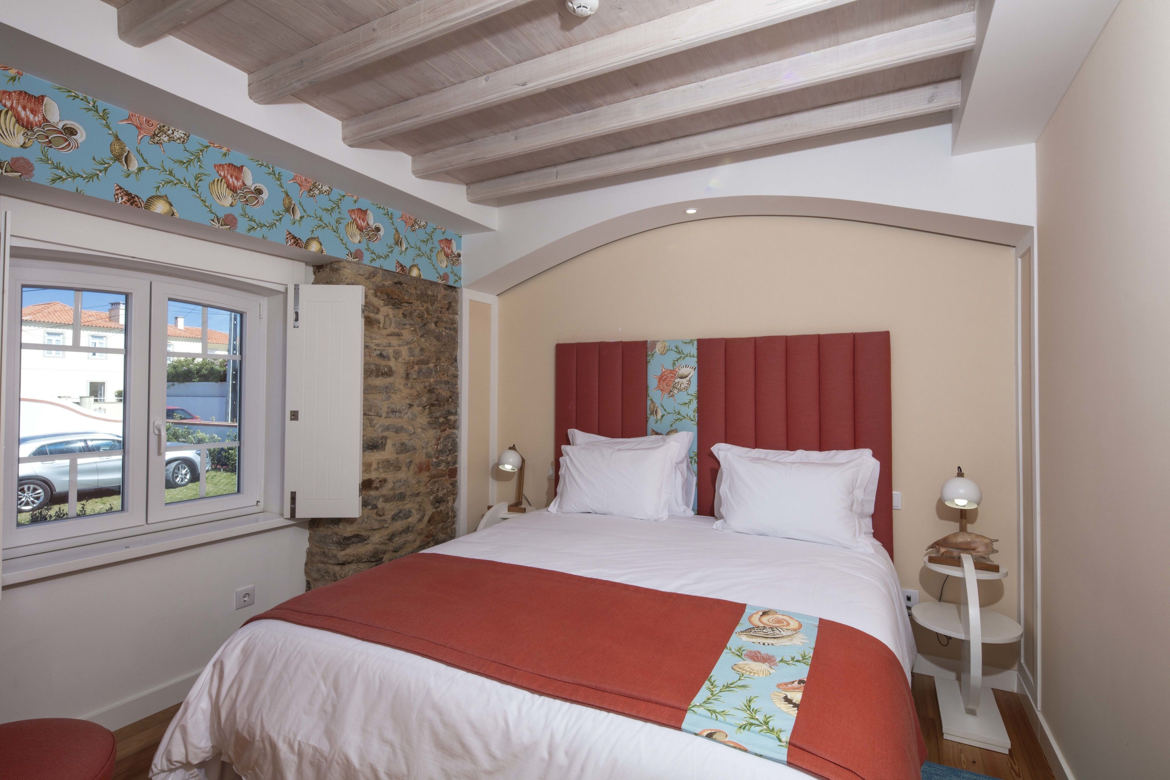 A bedroom with a bed, a window, a stone wall, and a red headboard.