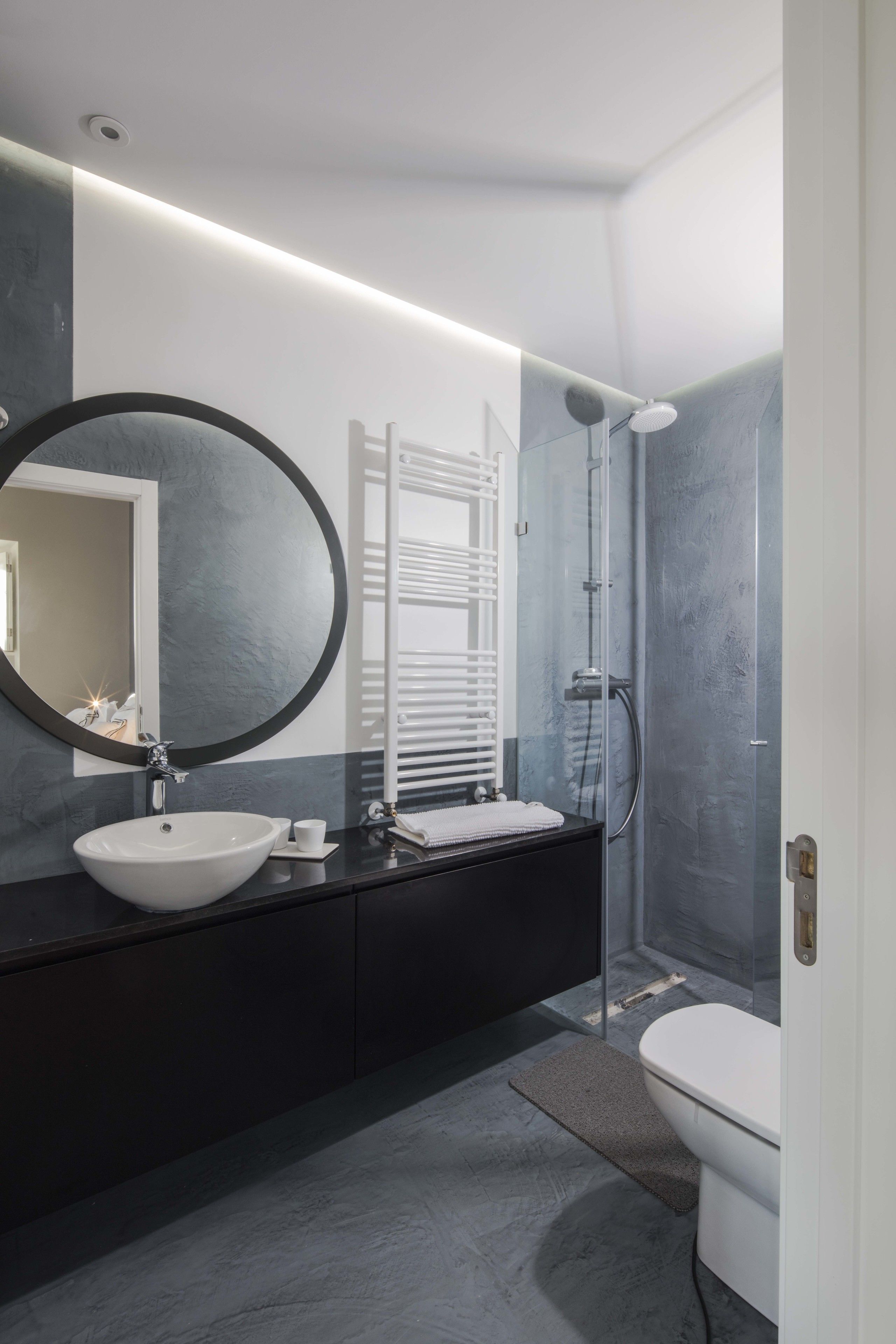 Une salle de bain moderne avec un grand miroir rond, un lavabo blanc et une douche à parois de verre.