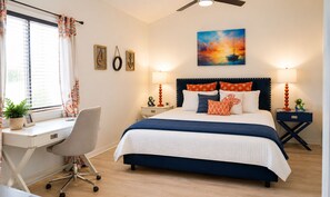 A bedroom with a bed, desk, chair, bedside tables, and artwork.