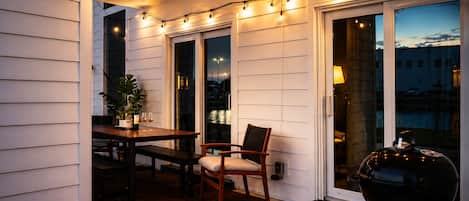 An outdoor patio area with a table and chairs, string lights, a grill, and a view of the cityscape.