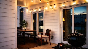 Area patio esterna con tavolo e sedie, luci decorative, un barbecue e vista sulla città.