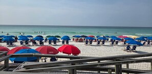 Una spiaggia con numerosi ombrelloni e sdraio, una passerella di legno e l'oceano sullo sfondo.