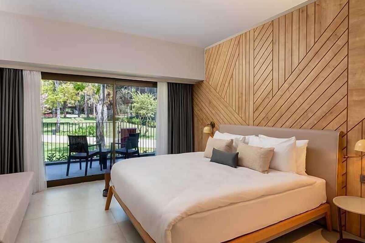 Un dormitorio moderno con una cama grande, un revestimiento de madera y vistas a un jardín a través de un ventanal corredero.
