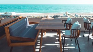 An outdoor seating area with wooden tables and chairs, overlooking a beach and the ocean. - Paloma Orenda - All inclusive (Manavgat)