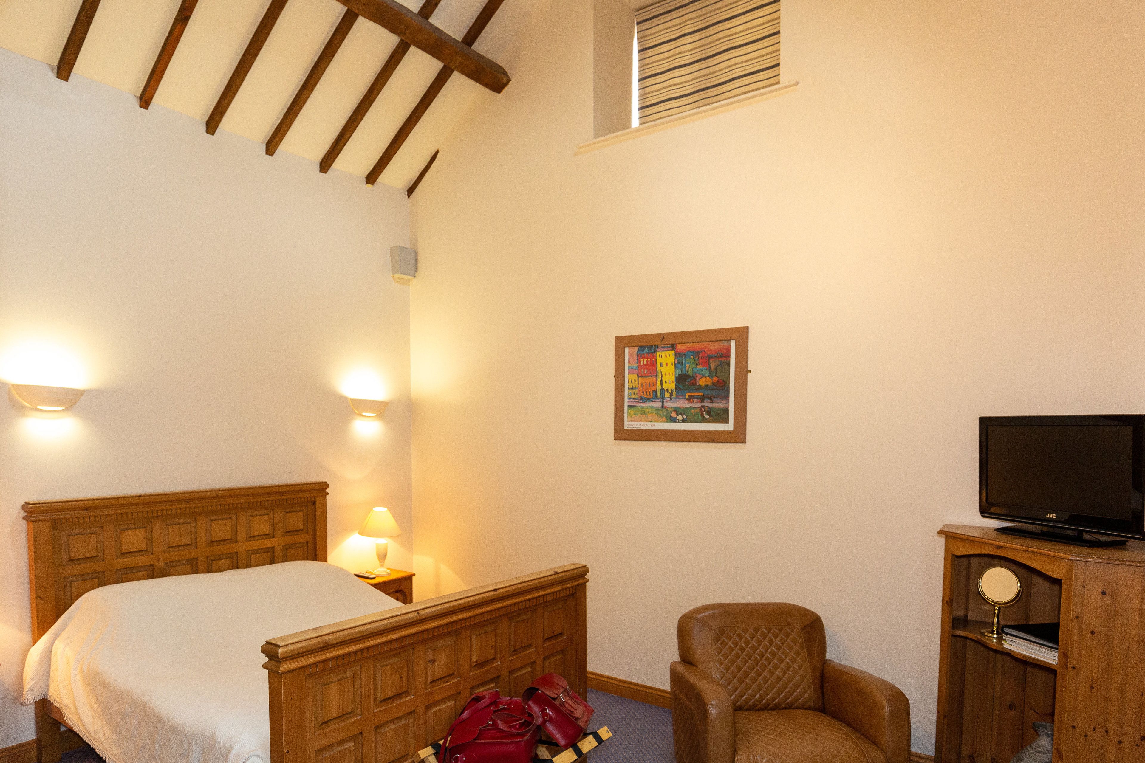 Ein Schlafzimmer mit einem hölzernen Bett, einem Sessel, einem Fernseher auf einem Holzschrank und einem Bild an der Wand.
