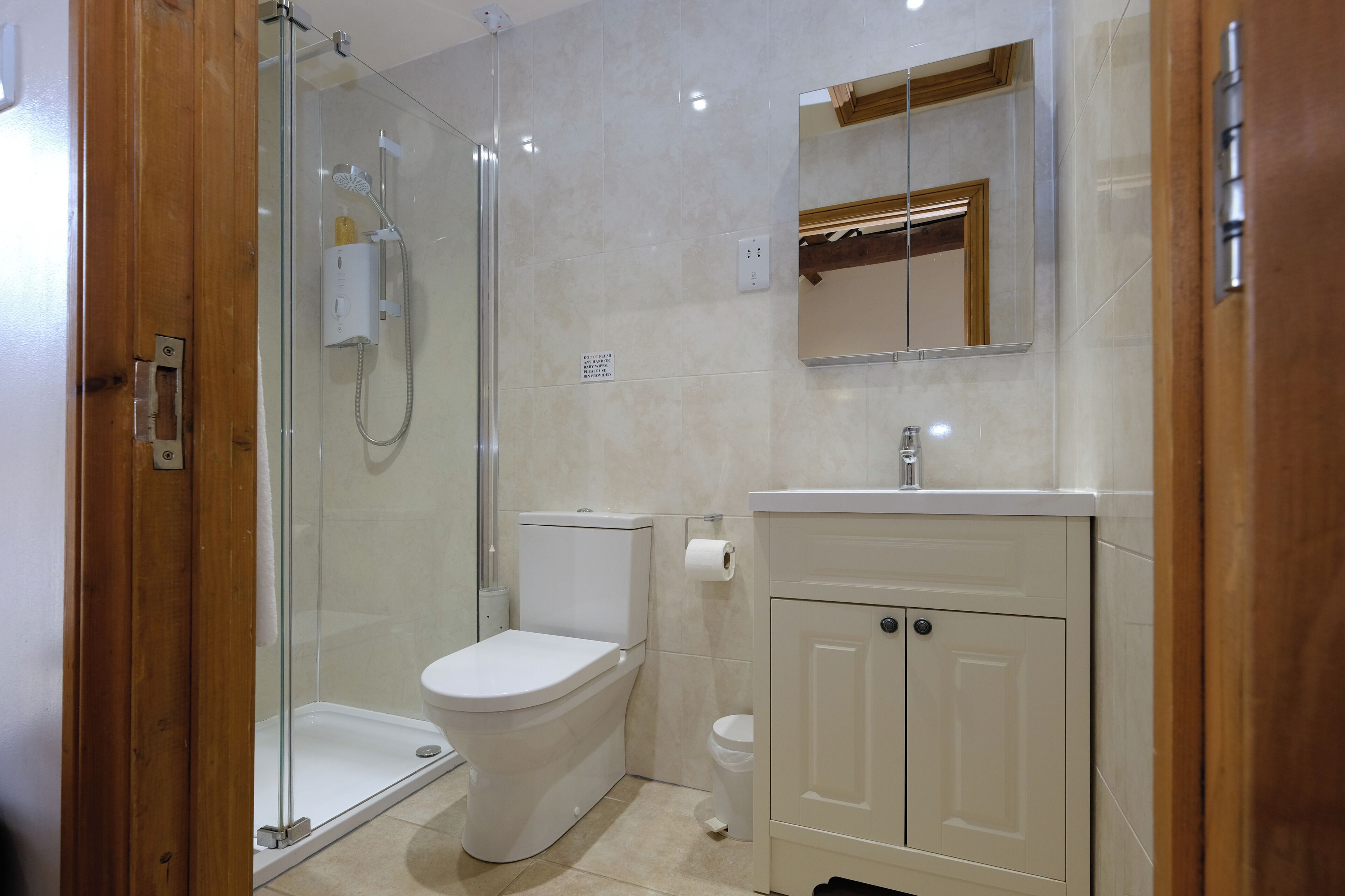 Un baño con mampara de vidrio, inodoro, lavabo con espejo y un armario.
