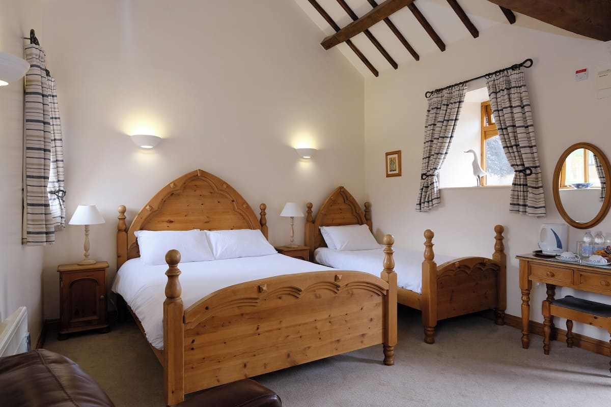 A bedroom with two wooden beds, a wooden dresser, a mirror, and a window with curtains.